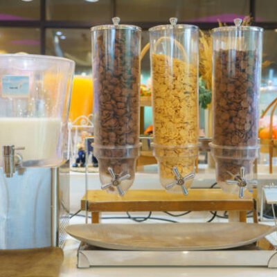 Choice of Cereals in hotel brakefast Breakfast setup featuring a cereal dispenser with three compartments filled with different types of cereals.