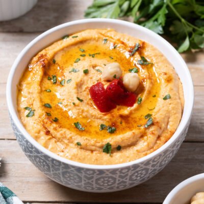 Roasted red pepper hummus in white bowl on wooden table Roasted red pepper hummus in white bowl on wooden table